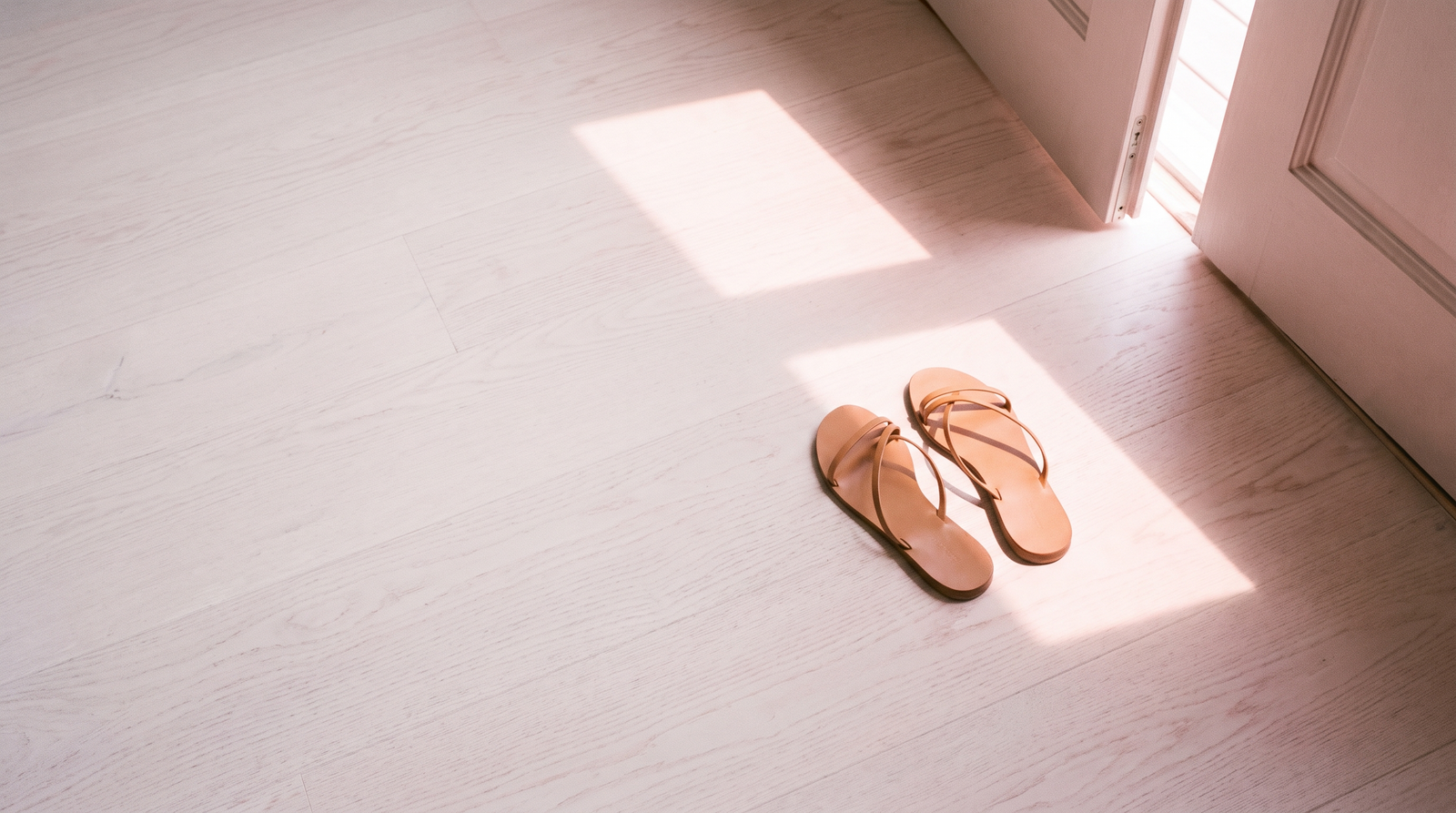 Tan leather sandals on a pale floor in a sunlit doorway